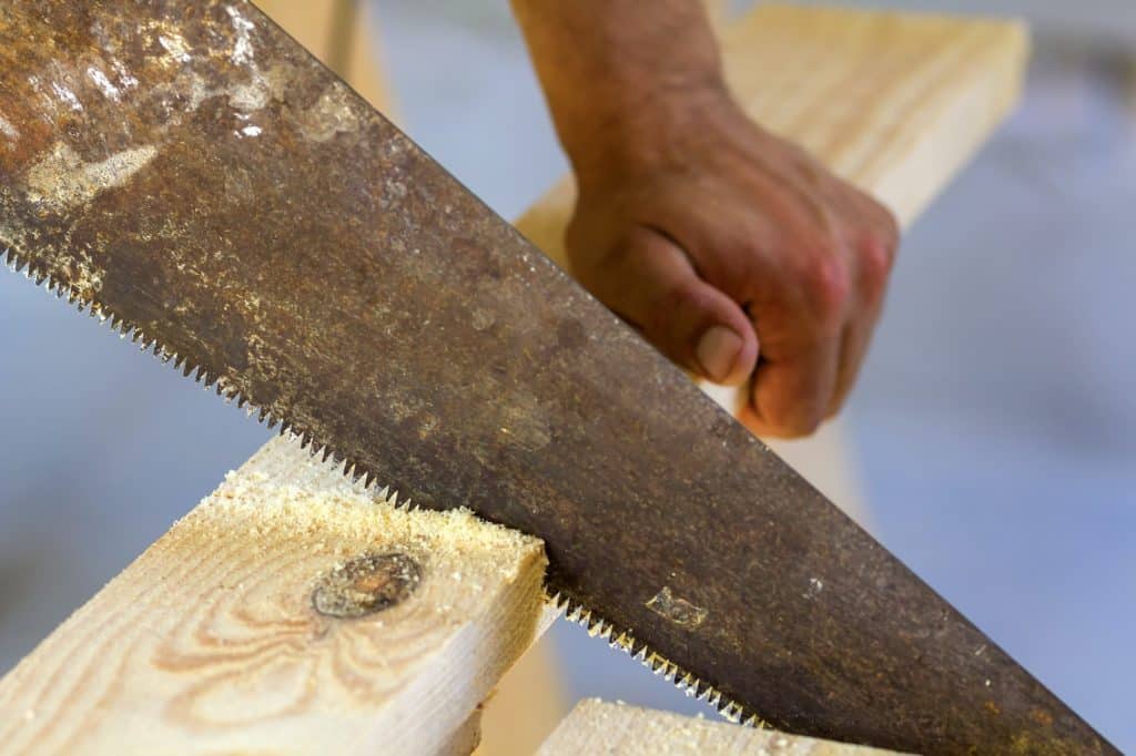 Carpenter hand with saw cutting wooden boards