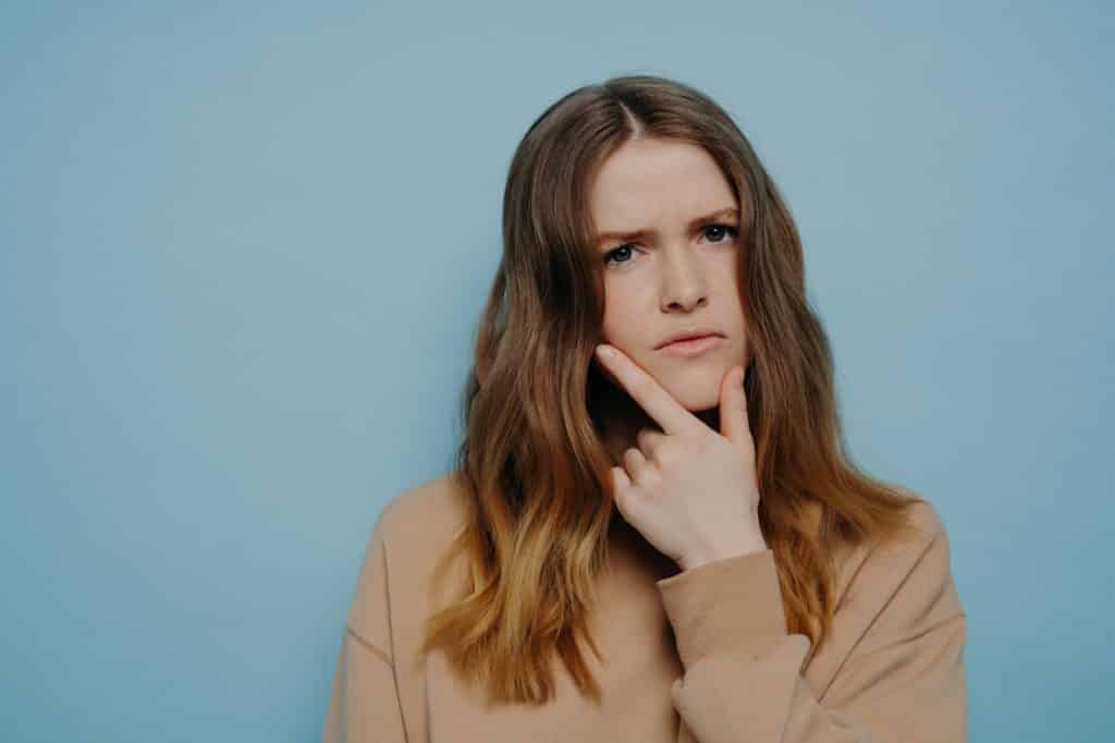 Confused young woman looking at camera standing over blue background