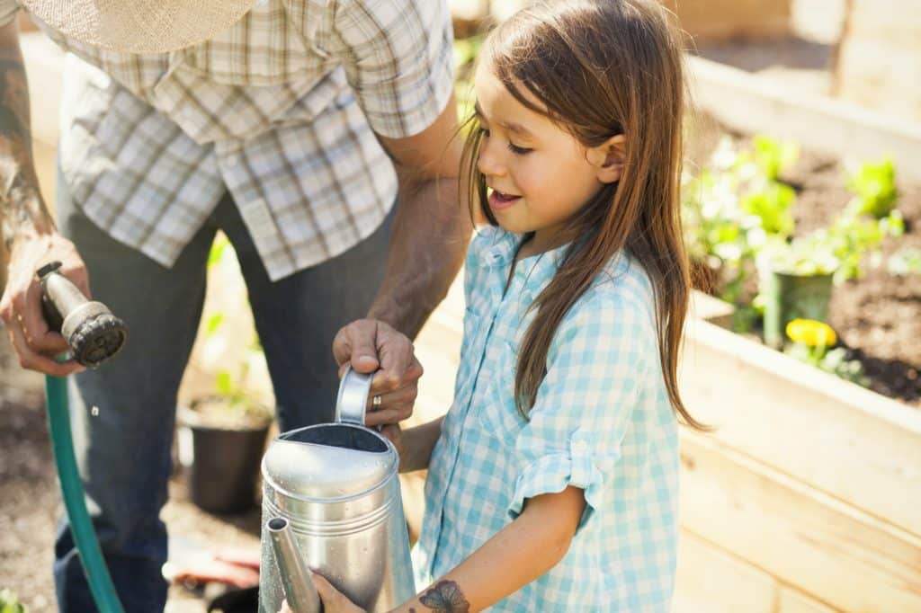 Father filling watering can for girl in community garden