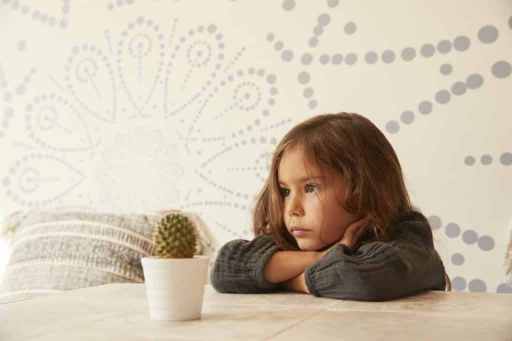 Young girl sitting at table, resting head on arms, pensive expression